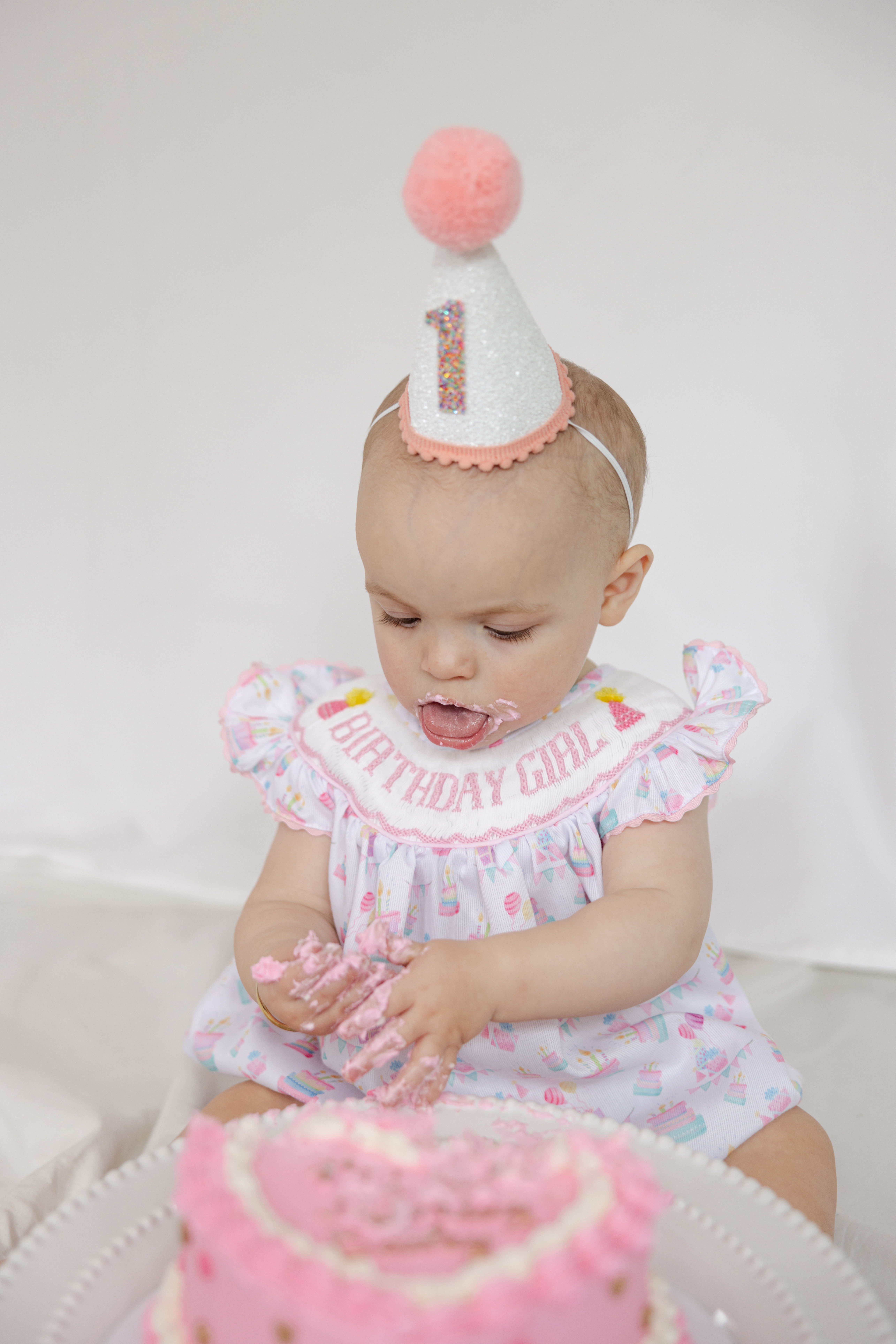 This studio photography session for a 1-year-old girl features a pink-themed setup and a playful smash cake moment. From her first messy bite to those precious giggles, these photos will capture the joy of her first birthday!