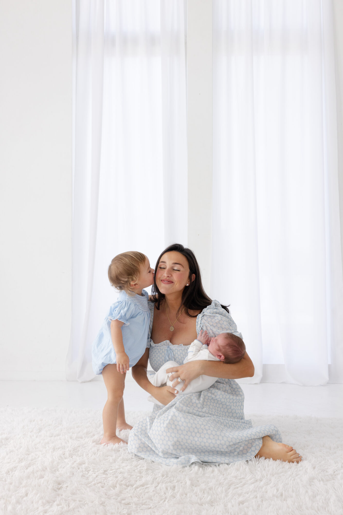 Big sister kissing mom while holding new baby brother