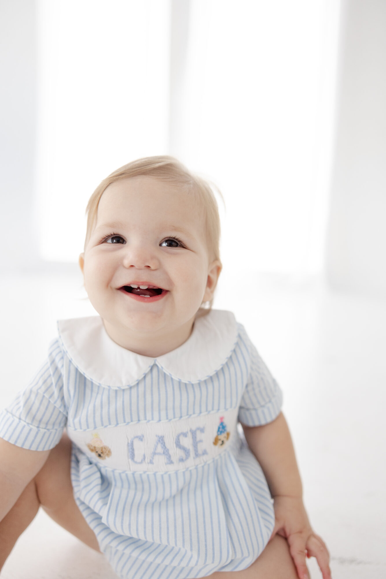 Smiling one year old boy wearing blue overalls during a Houston milestone photography session.