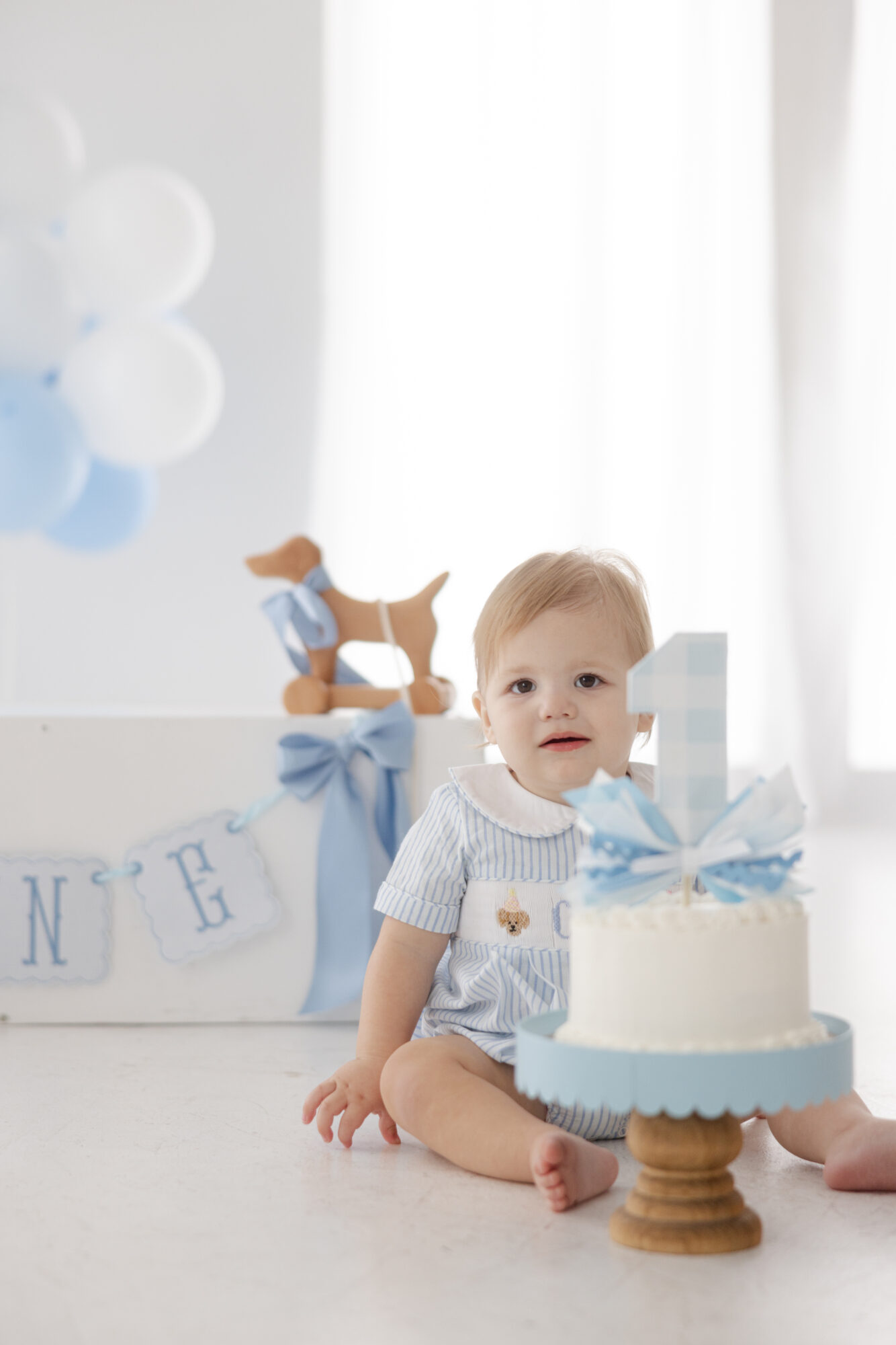 Baby boy sitting next to his birthday cake during a Houston cake smash photography session. 