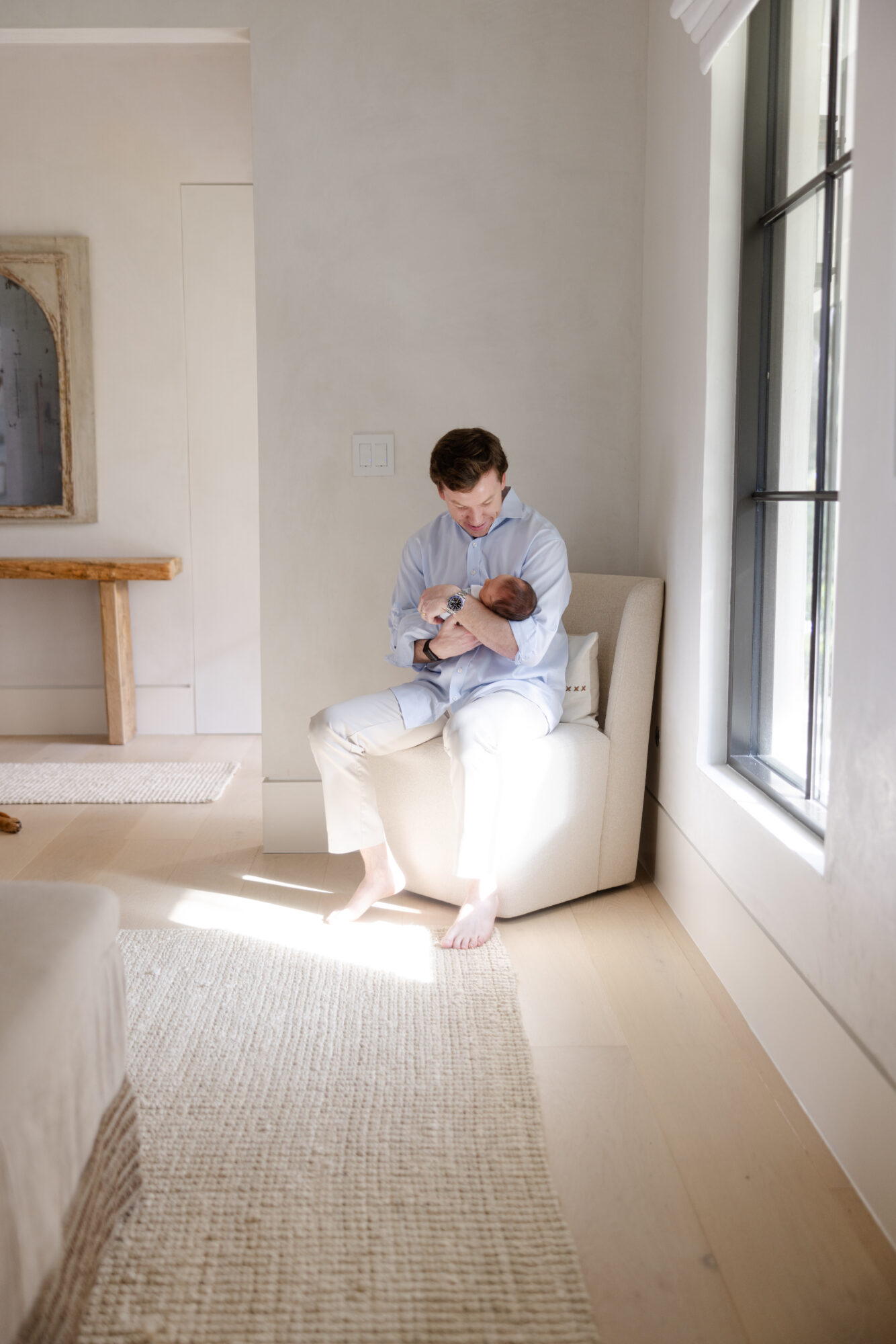 Dad cuddling newborn son in a sunlit room during a Houston lifestyle newborn session.